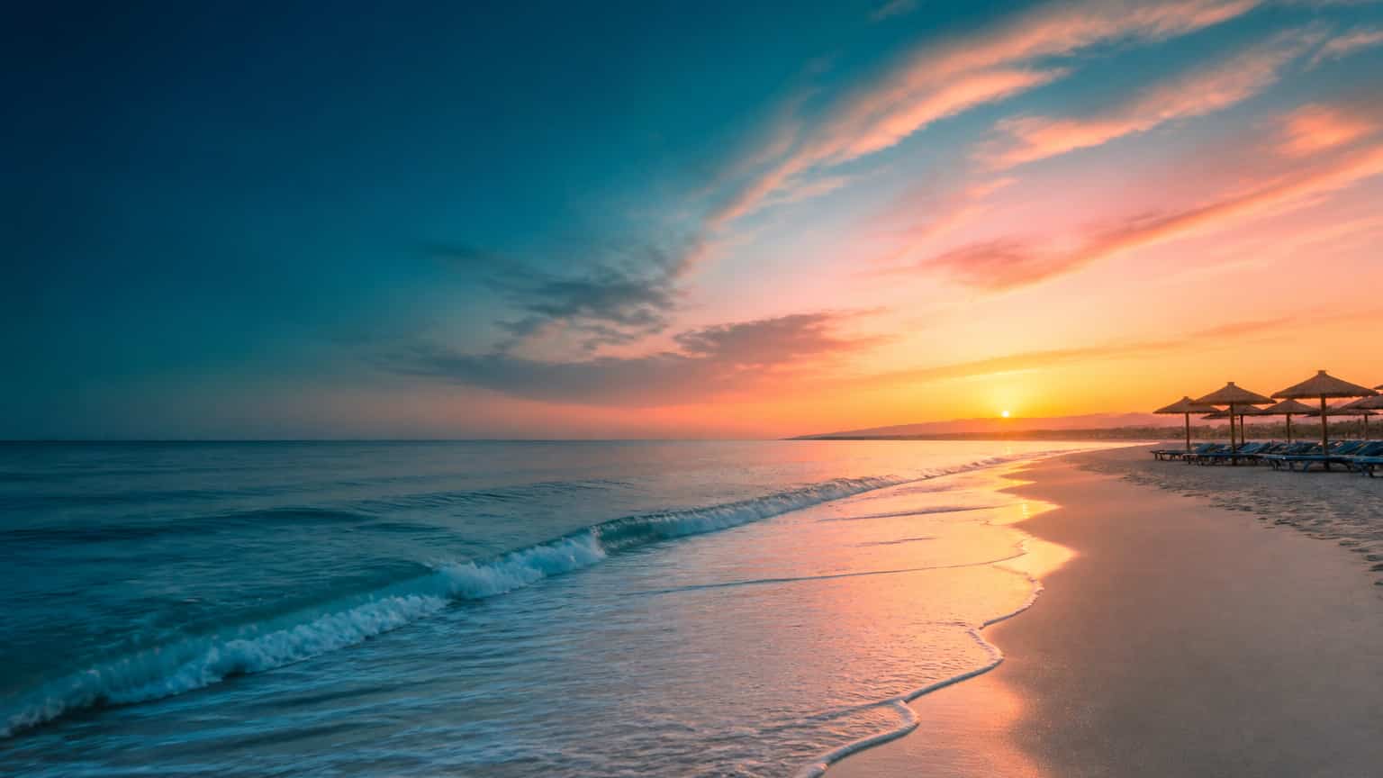 A broad Atlantic beach under a coral and golden dawn